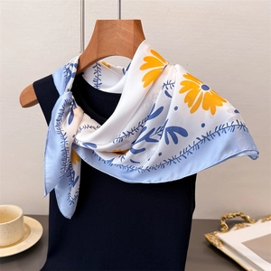 Detailaufnahme eines Seidenschals mit gelben Gänseblümchen und blauen Ranken auf Bügel
