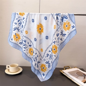 Nahaufnahme von Seidenschal mit gelben Gänseblümchen und blauem Rand am Kleiderbügel