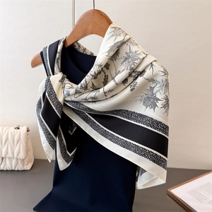 Silk-like square scarf with grey floral prints and striped edges on a wooden hanger