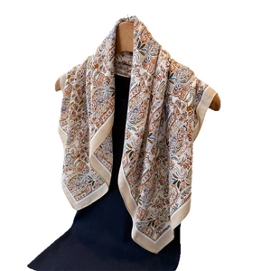 Elegant paisley print silk scarf in beige and brown hanging on a wooden hanger