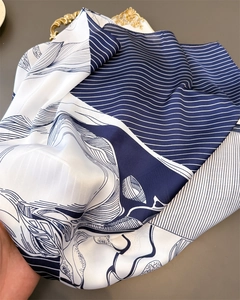 Detailed view of folded silk scarf featuring blue stripes and elegant wavy patterns