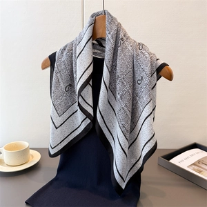 Detail of soft black and white paisley pattern scarf on a wooden hanger against white wall