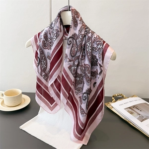 Detail of silk-like paisley square scarf styled on a white hanger with luxury accessories