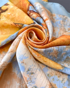 Gros plan d'un foulard en soie avec imprimé artistique nature tons orange et bleu