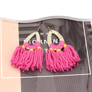 Detailed close-up of bohemian woven straw earrings with vibrant pink yarn tassels