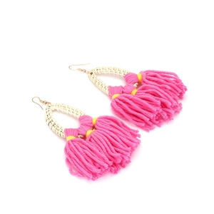 Detailed view of handmade rattan earrings with bright pink tassels and golden metal hooks
