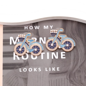 Détail de boucles d'oreilles vélo en émail bleu avec perles sur fond de magazine de mode
