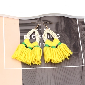 Detail of bohemian handmade yellow tassel earrings with woven straw accents on a stylist backdrop