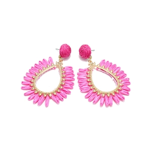 Détail de boucles d'oreilles bohèmes en raphia rose avec cadres en métal doré