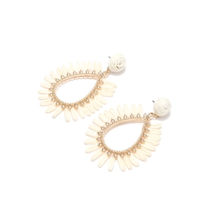 Détail de boucles d'oreilles en raphia bohème montrant la texture tissée ivoire et l'or