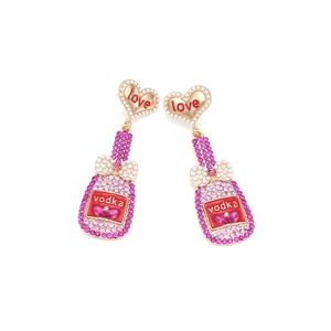 Détail de boucles d'oreilles cœur avec perles et pendentifs bouteille en strass rose