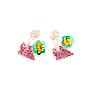 Détail de boucles d'oreilles dorées avec cristaux roses et robe fleurie en paillettes