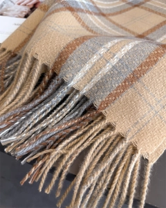 Detalle de bufanda de cuadros con patrones de color camello y gris y elegantes flecos largos