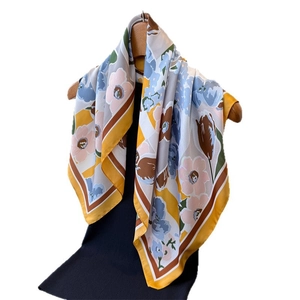 Floral print silk scarf with yellow borders hanging on a wooden hanger over dark clothing