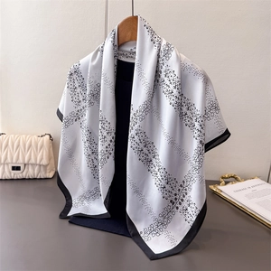 Elegant black and white floral faux silk scarf hanging on a wooden hanger with silk texture
