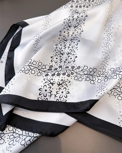 Detail of silk-feel scarf featuring black floral patterns and border on white background