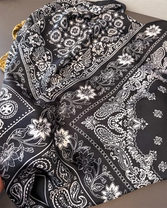 Detail of silk satin scarf with paisley prints and soft draped texture on grey surface