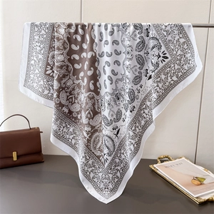 Brown and white paisley satin square scarf displayed with a luxury handbag and gold tray