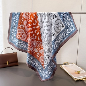 Elegant paisley satin square silk scarf in orange and navy blue, hanging on a display rod