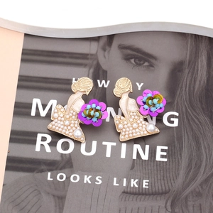 Détail de boucles d'oreilles silhouette femme avec perles blanches et fleurs à paillettes