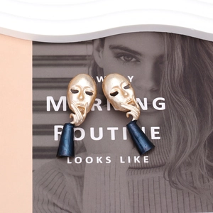 Abstract face earrings with gold mask and blue teardrop charm on fashion magazine