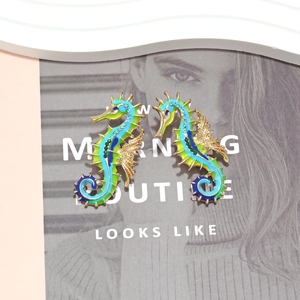 Colorful enamel seahorse earrings with crystals on a textured magazine background