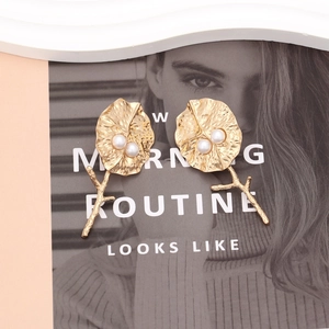 Boucles d'oreilles feuilles dorées avec perles sur fond de magazine de mode élégant