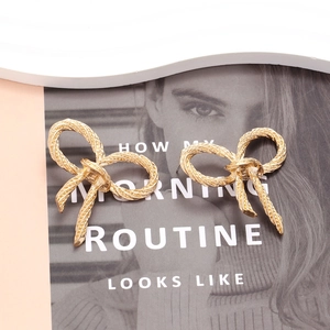 Elegant gold bow earrings with twisted rope texture presented on a fashion magazine