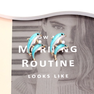 Cute blue enamel dolphin stud earrings with white pearl detail on fashion magazine background