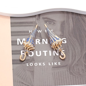 Boucles d'oreilles parapluie avec cristaux bleus et placage or sur fond de magazine