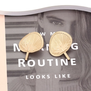 Elegant gold fan shaped alloy stud earrings with textured finish on magazine background