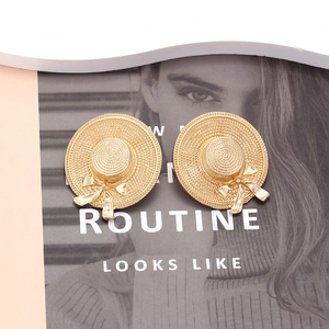 Elegant gold straw hat earrings with bow design shown on a fashion magazine background