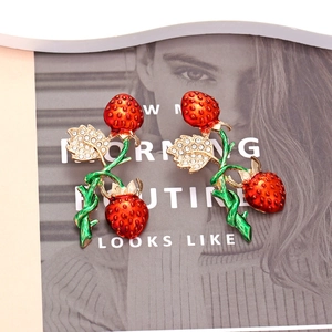 Sparkling strawberry enamel earrings with green rhinestone leaves on magazine background