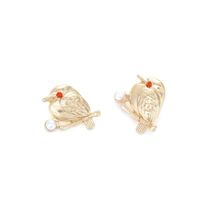 Boucles d'oreilles oiseau dorées avec perle et strass rouges sur fond blanc