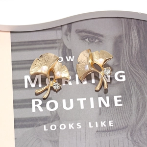Golden ginkgo leaf stud earrings with white faux pearls and crystals on soft background