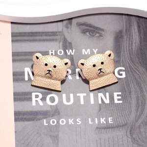 Boucles d'oreilles ours dorées mates avec détails en émail noir sur fond de magazine