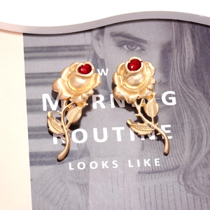 Baroque gold rose earrings with red gemstone center on a stylish magazine background