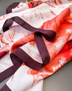 Detalle de bufanda de seda con estampado de hojas naranjas y bordes en marrón oscuro
