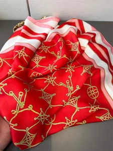 Macro detail of red faux silk scarf showing golden nautical rope print and satin luster