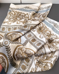 Close-up of luxury faux silk scarf featuring golden Baroque scrolls and blue Greek Key border