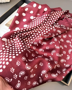 Detailed view of dark red paisley and polka dot silk scarf draped on a display tray
