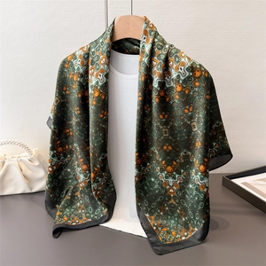 Fashionable dark green satin scarf with orange geometric dot print on a wooden hanger