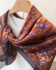 Detail view of abstract eye print satin scarf with black borders on a wooden hanger