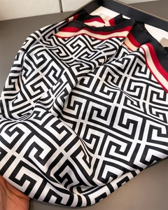 Close-up of geometric meander print satin scarf with tri-color striped border detail
