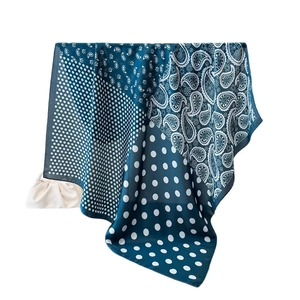 Elegant navy blue paisley and polka dot silk scarf draped next to a stylish white handbag