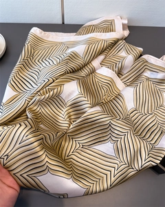 Detailansicht eines Satin-Seidenschals mit goldenem und schwarzem Retro-Druckmuster