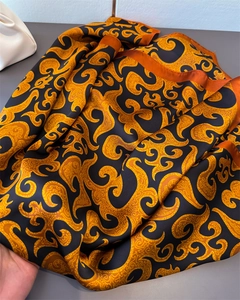 Macro detail of high-quality satin silk scarf with gold scroll patterns and orange hem