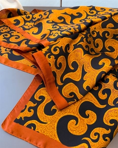 Close-up of silk-textured scarf with ornate baroque patterns in orange and black