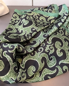 Detailed close-up of folded satin scarf showing green scroll patterns on black fabric