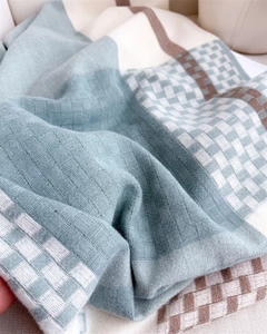 Close-up of woven plaid texture in blue and beige cashmere-like scarf with soft fringe